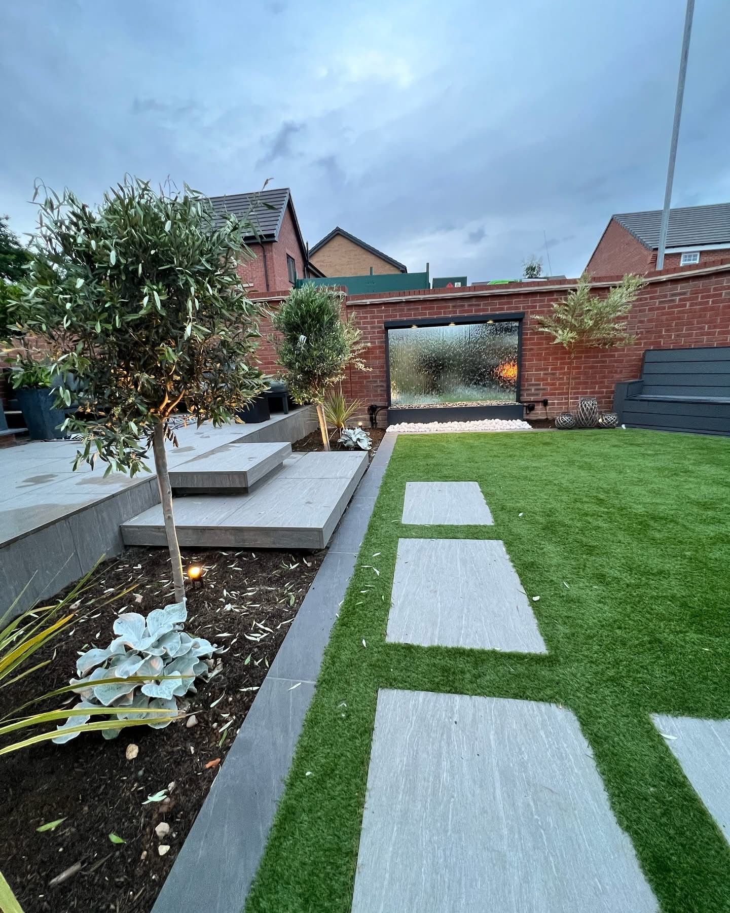 Garden with olive tree, stepping stones and artificial grass